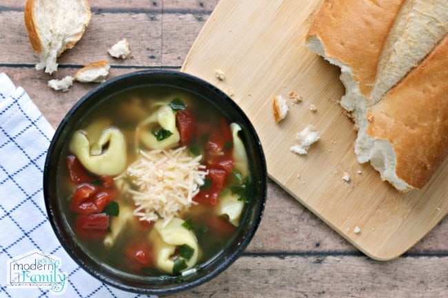 A bowl of tortellini soup with a loaf of bread beside it.