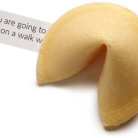 A close up of a fortune cookie with a fortune paper beside it.