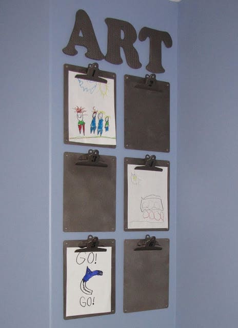 Clipboards attached to a wall with art clipped on them.