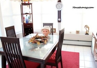 A  dining room table with a doll sitting in a chair.