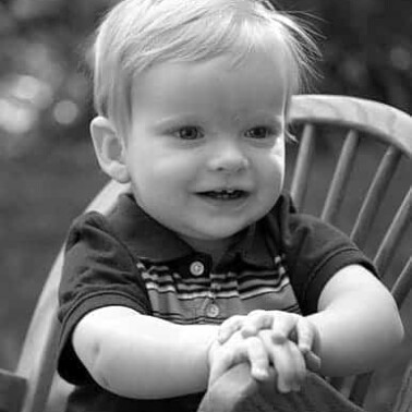A small child sitting in a rocking chair with text above him.