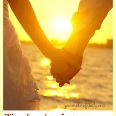 An image of the sun shining between a couple's hands as they walk down the beach.