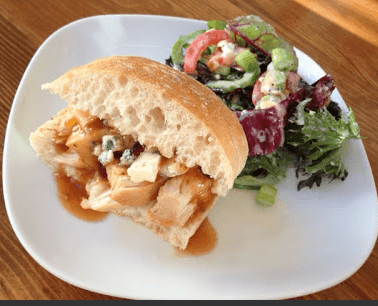 A BBQ chicken sandwich and salad on a white plate.