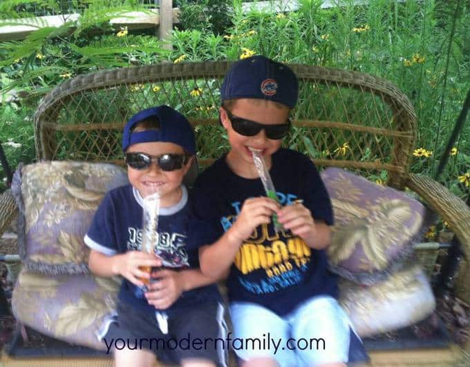 Two kids sitting on a porch swing eating a cold snack.