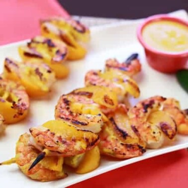 Shrimp on skewers with a cup of dip beside them.