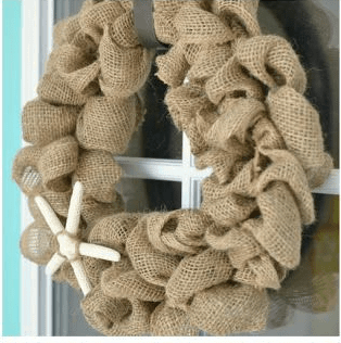 A burlap wreath on a front door with a sand dollar on it.
