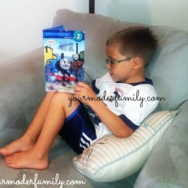 A boy sitting on a couch reading a book.