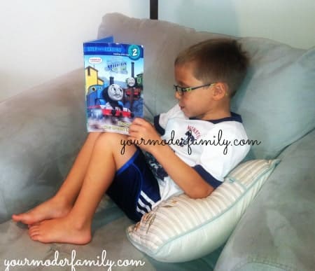 A boy sitting on a couch reading a book.