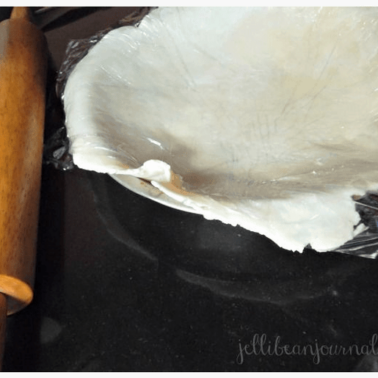A pie pan with raw dough in it and a rolling pin beside it.