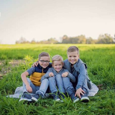 Tree boys sitting close together in a field.