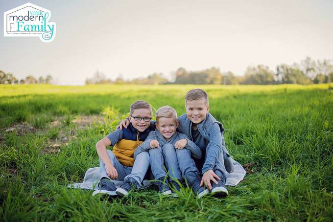 Three boys sitting close together in a field of grass.