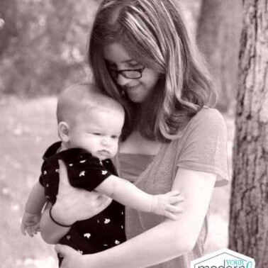 A woman holding a baby in her arms next to a tree.