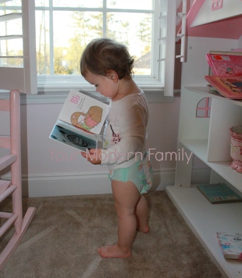 A little girl standing in front of a window looking at a book.