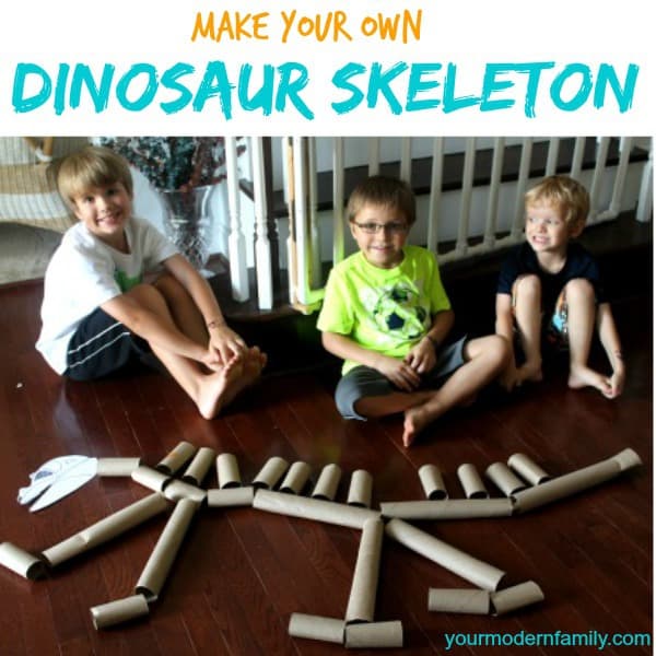 Three children sitting on the floor building a dinosaur out of toilet paper rolls.