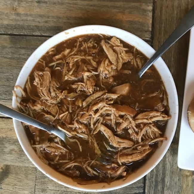 A top view of a shredded pork loin  cooked in french onion soup with two utensils in the bowl.