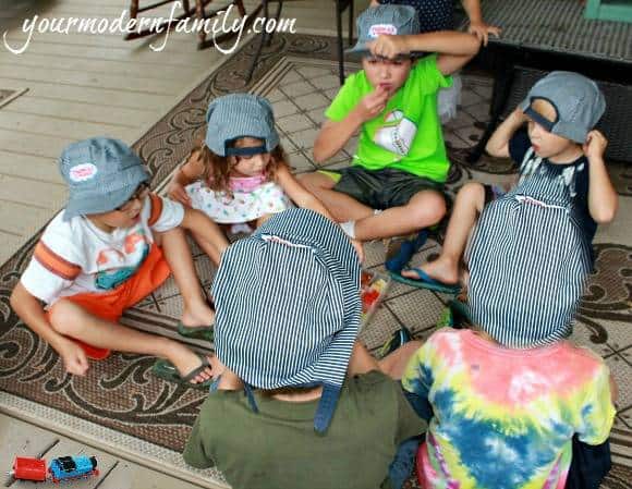 A group of kids sitting in a circle wearing train engineer hats.