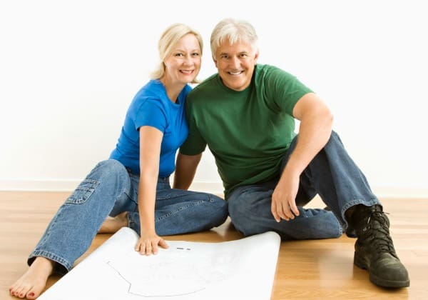 Middle-aged couple sitting on floor with architectural blueprints.