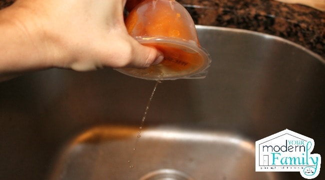 A hand draining juice from a container of fruit snacks.