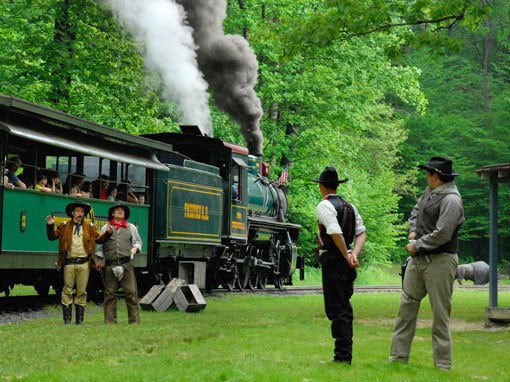 A group of people near a train with smoke coming out of it.