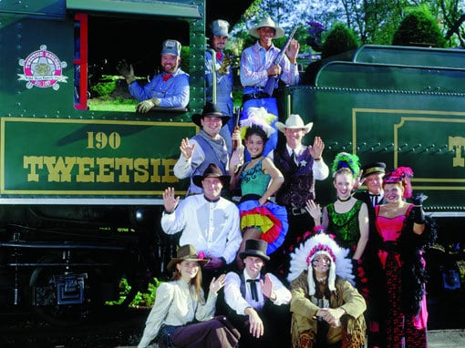 A group of people standing in front of a train engine posing for the camera.