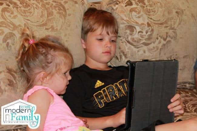 Two kids sitting on a couch looking at a laptop.