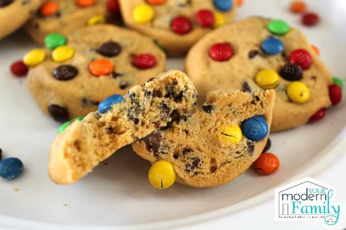 A close up of a plate of M&M cookies with one cookie cut in half.
