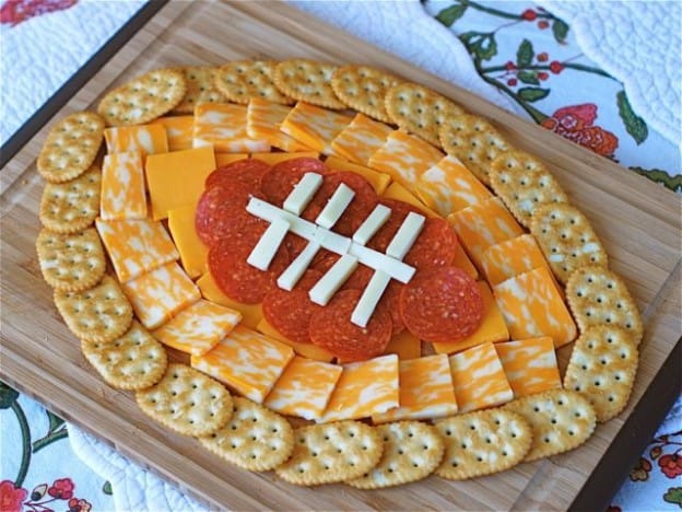 A plate of food shaped like a football, with cheese, crackers and pepperoni for a football party.
