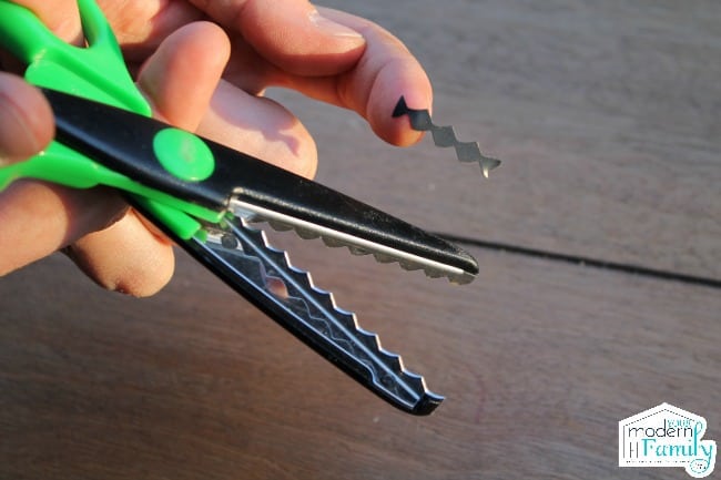 A pair of scissors with a small zig zag cut piece of paper in an adults hand.