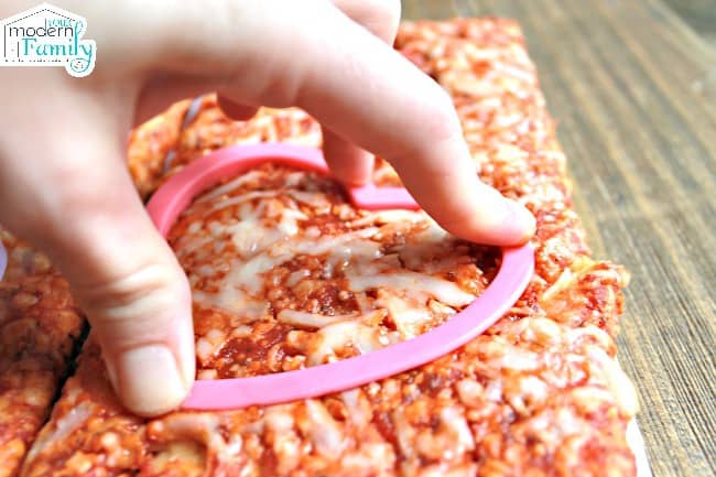 A person using a heart shaped cookie cutter to cut the pizza.