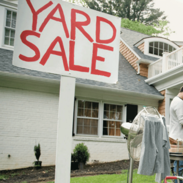A person standing in front of a house having a yard sale.