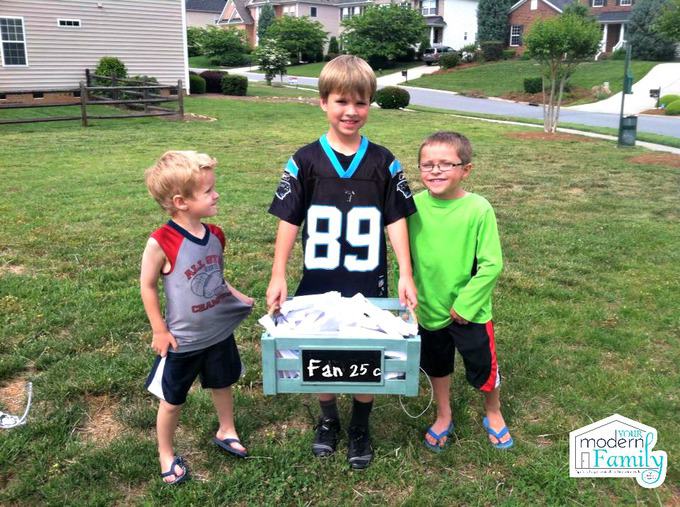 A three boys that are standing in the grass holding a box.
