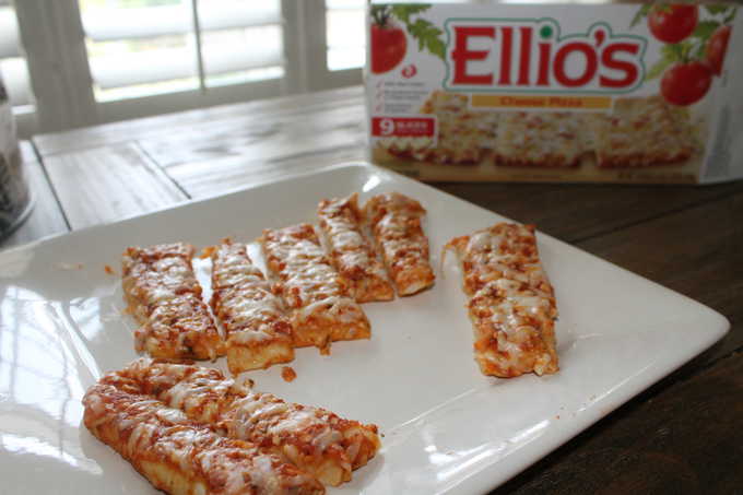 A plate with slices of pizza with Ellio\'s Pizza box behind them.
