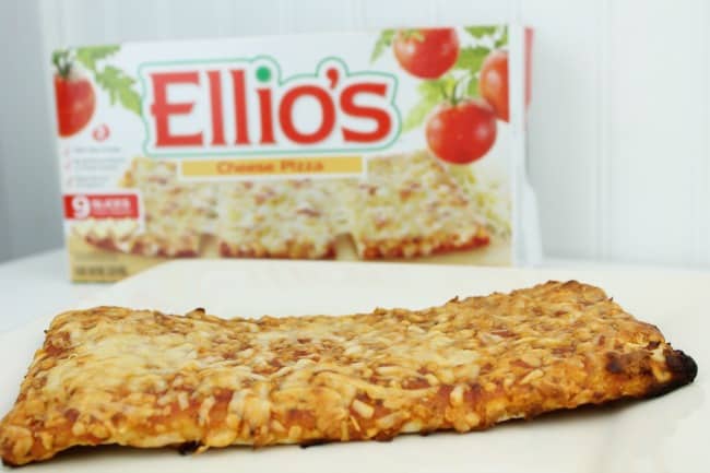 A slice of pizza on a plate with a Ellio\'s pizza box behind it.