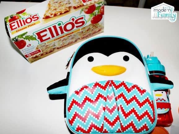A penguin themed lunch box with Ellio\'s pizza box behind it.