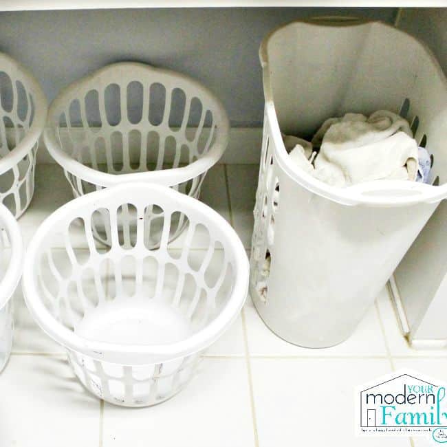 A large laundry basket filled with dirty clothes and four empty laundry baskets sitting beside it.