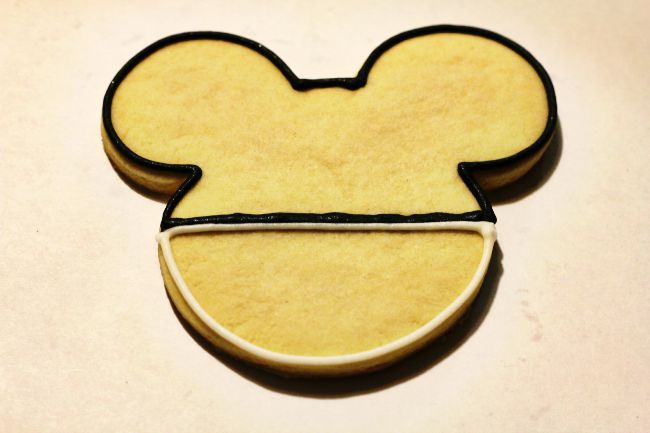 A Mickey Mouse shaped cookie that is partially iced.
