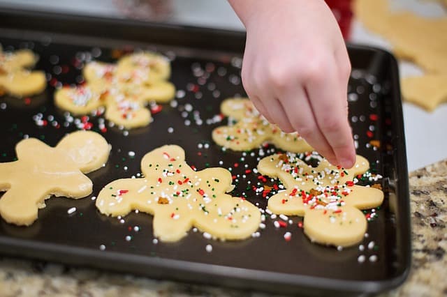 A hand adding sprinkles to cookies.