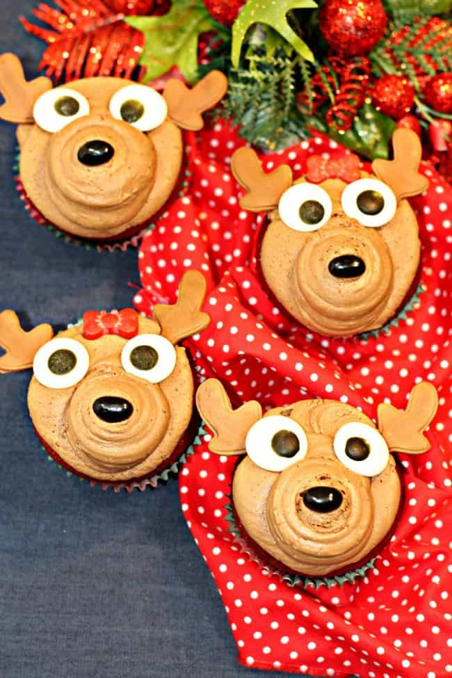 Reindeer themed cupcakes resting on a Christmas table cloth.