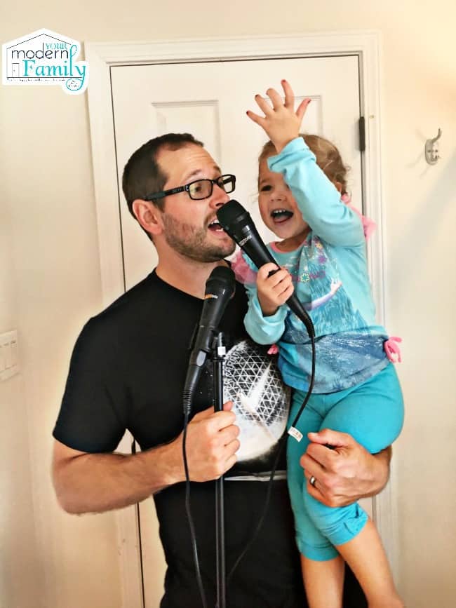 A man holding a microphone and a little girl, both singing.