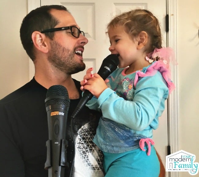 A man holding a little girl while she sings into a microphone.