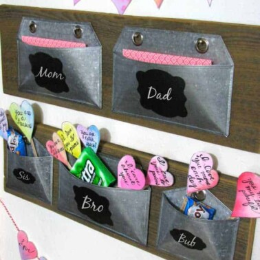 A display of silver envelopes attached to a wall with names on each one and Valentines Day items in each one.