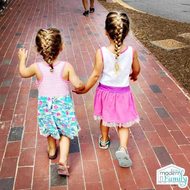 Two little girls walking down a brick side walk.