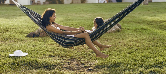 A woman and a little girl sitting in a hammock holding hands.