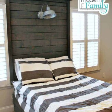 A bedroom with a bed with a wooden headboard between two windows.
