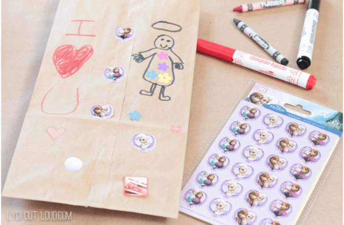 A brown bag with a child\'s drawing on it with stickers and makers beside it.