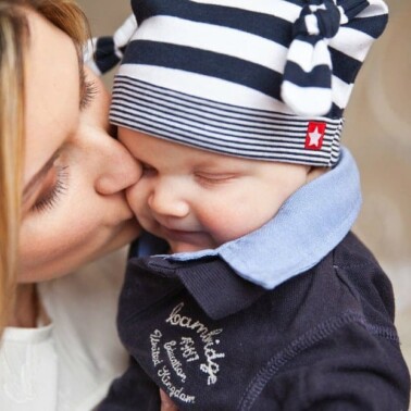 A close up of a woman kissing a baby wearing a winter hat.