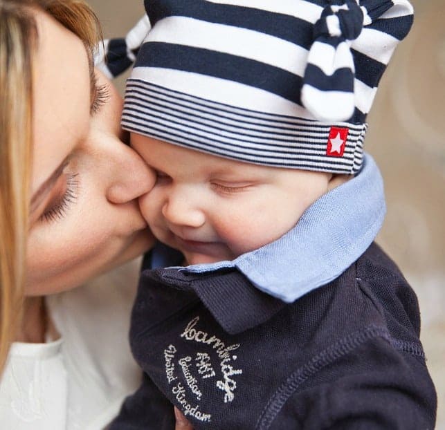 A close up of a woman kissing a baby wearing a winter hat.