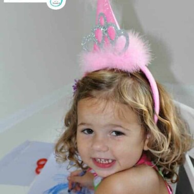 A little girl wearing a pink birthday hat while coloring pictures.