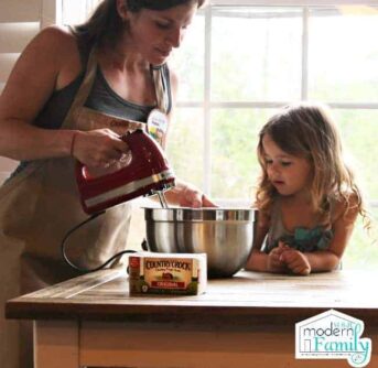 A woman and child mixing cookie dough in a metal bowl.