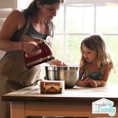 A woman and child mixing cookie dough in a metal bowl.